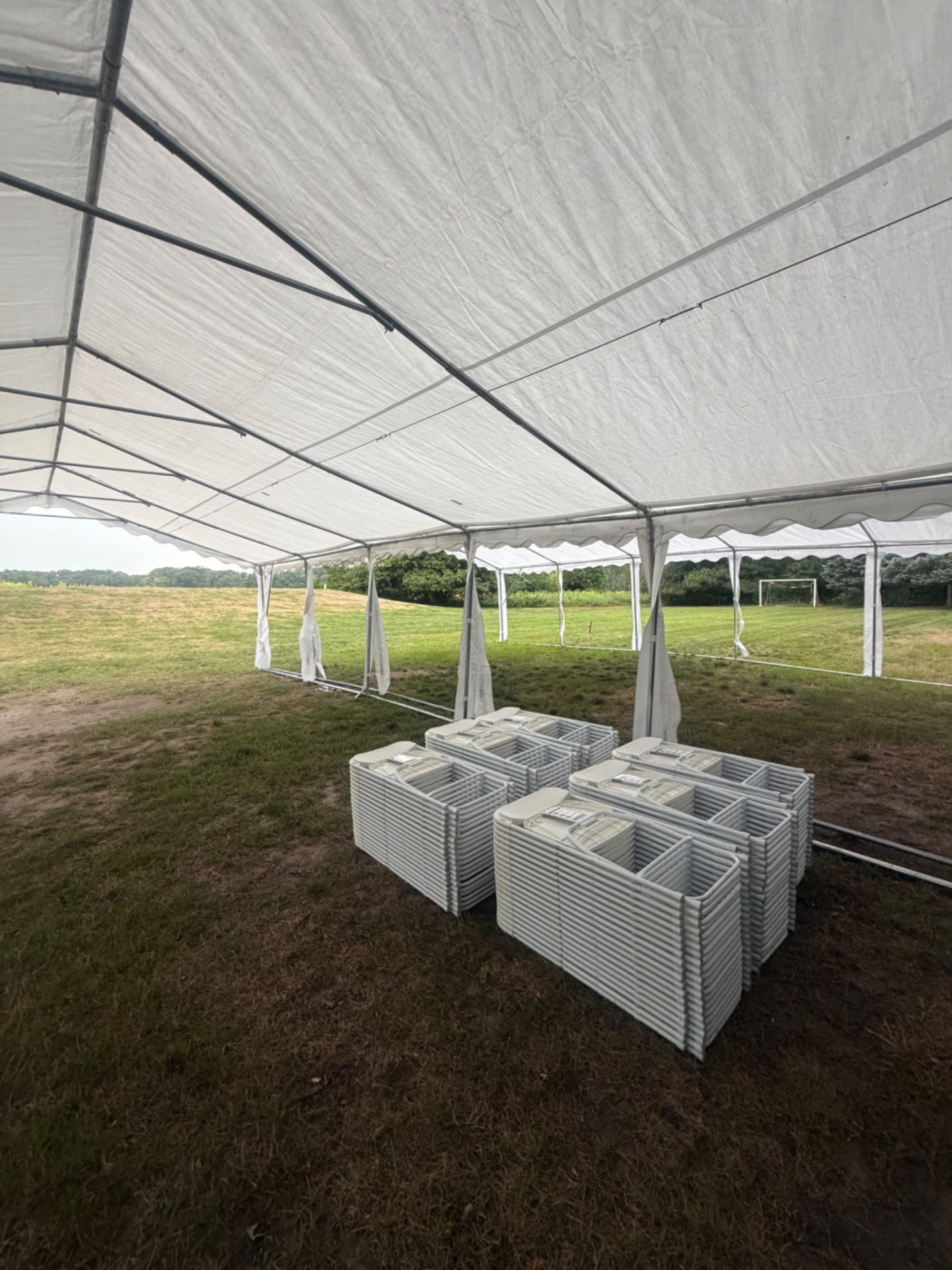 White folding chairs stacked under a large event tent on a grass field