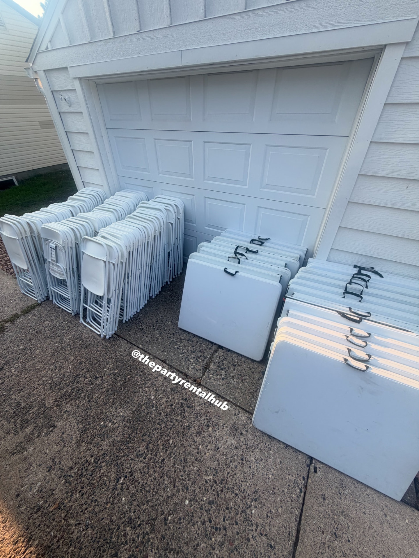 Rows of folding tables and white chairs staged outside a garage