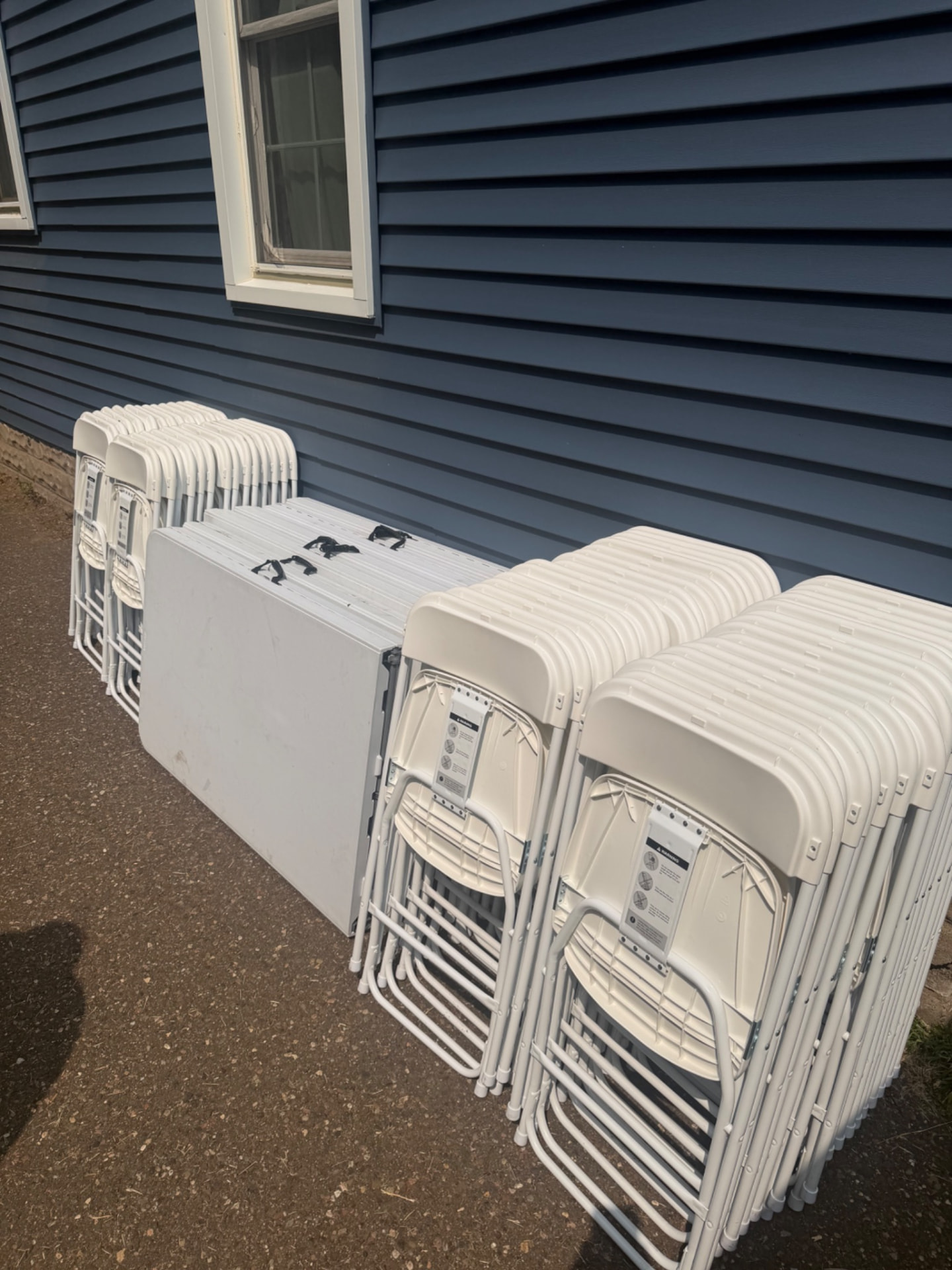 Folding tables and white chairs lined up along a driveway