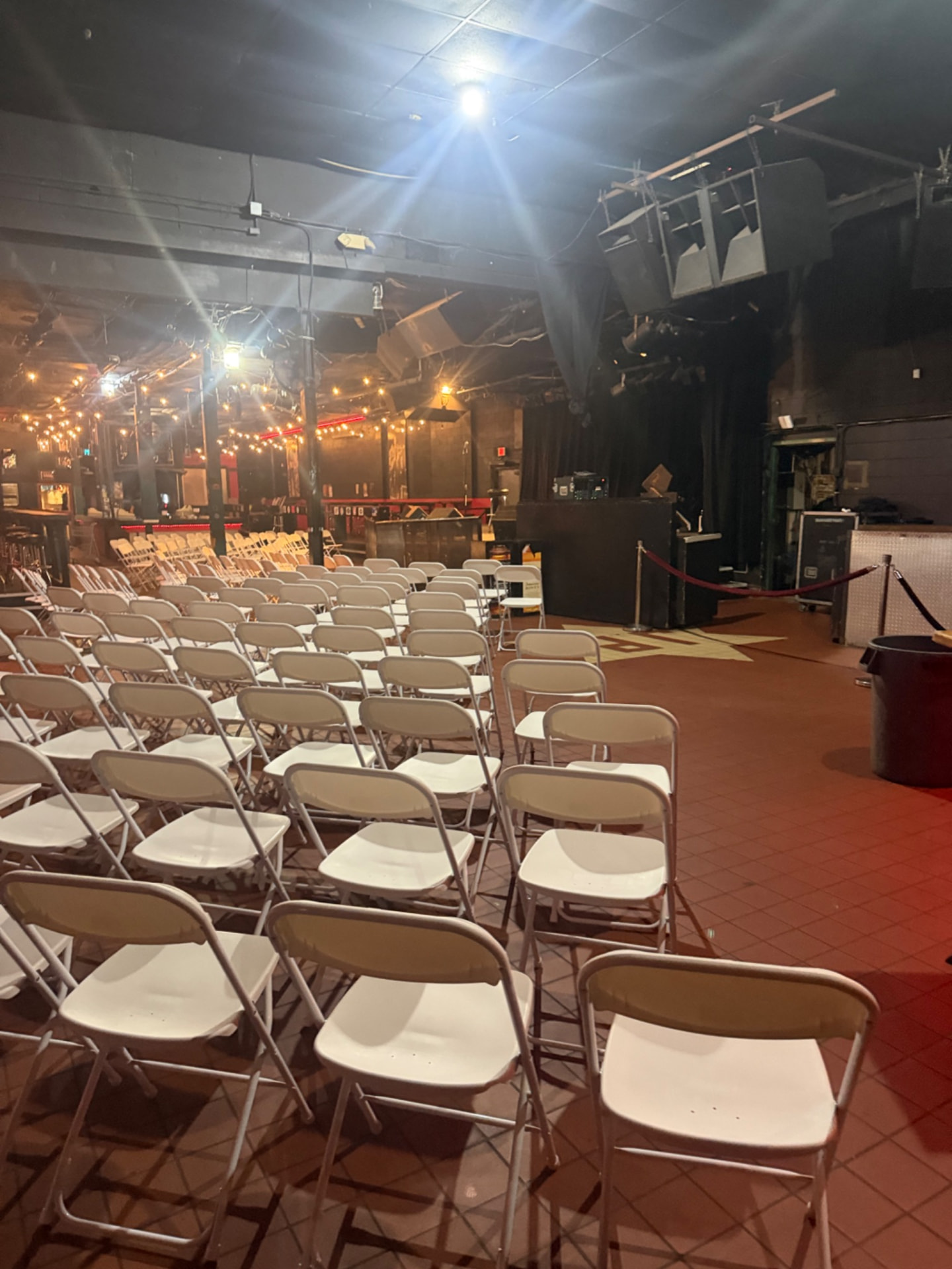 Rows of white folding chairs set up inside a venue with stage lighting