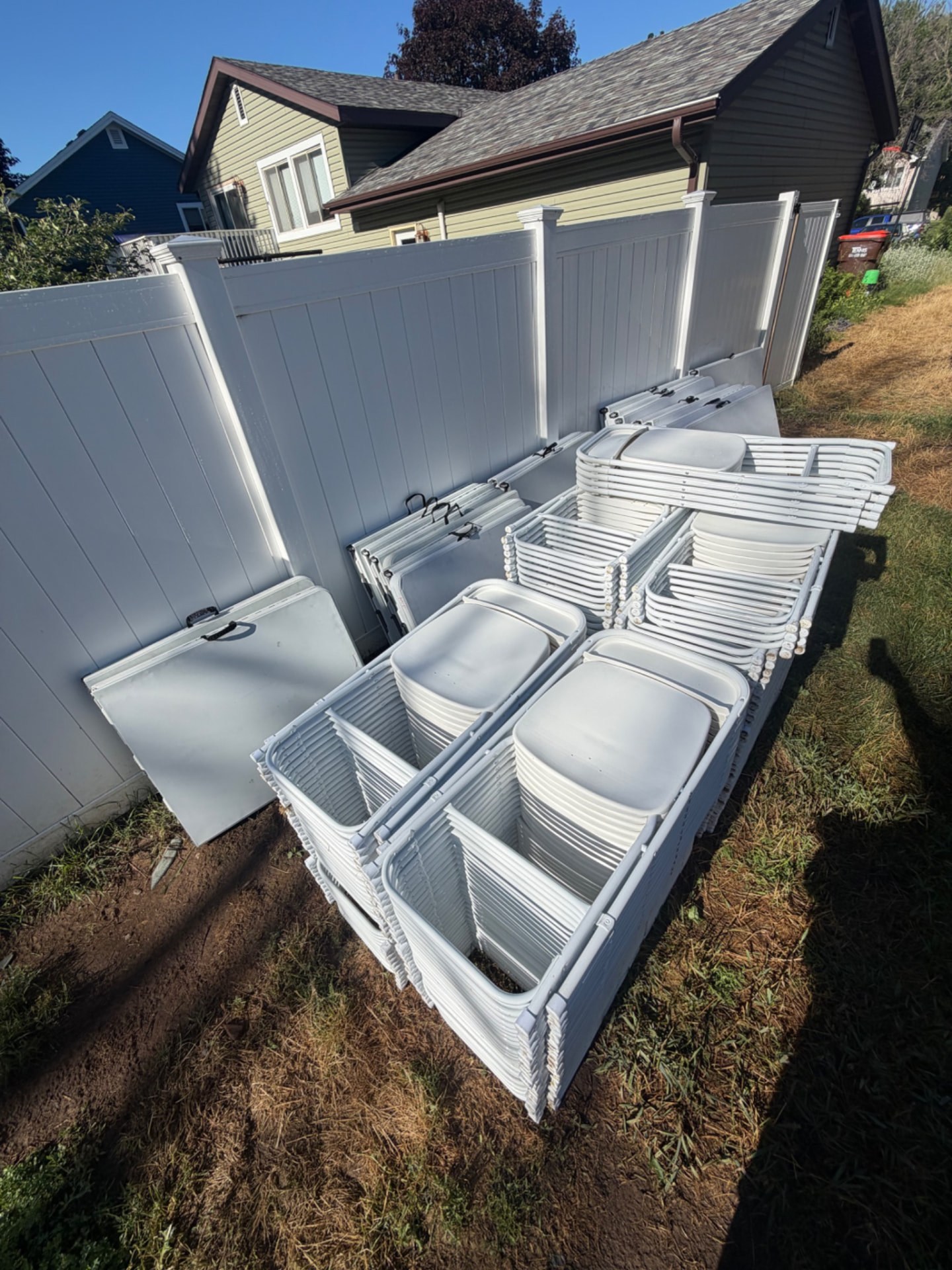 Stacks of folding tables and white chairs delivered alongside a home