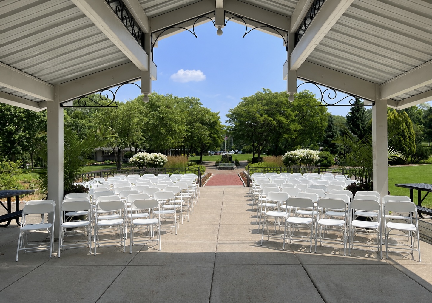 White folding chairs arranged for a ceremony under a park pavilion