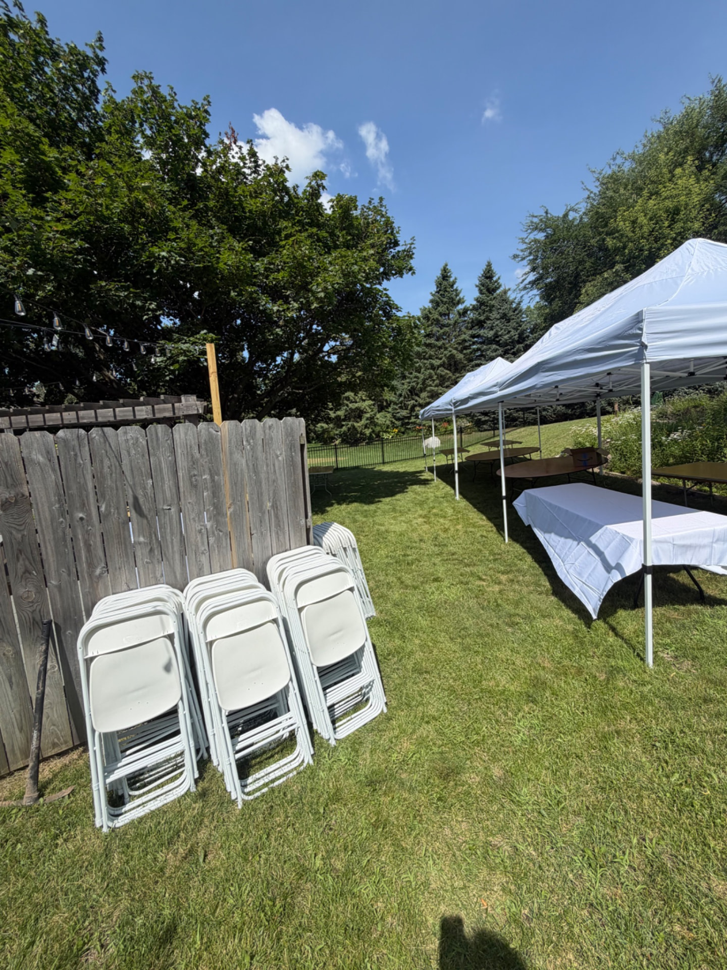 Backyard party with tents, banquet tables and stacks of white folding chairs