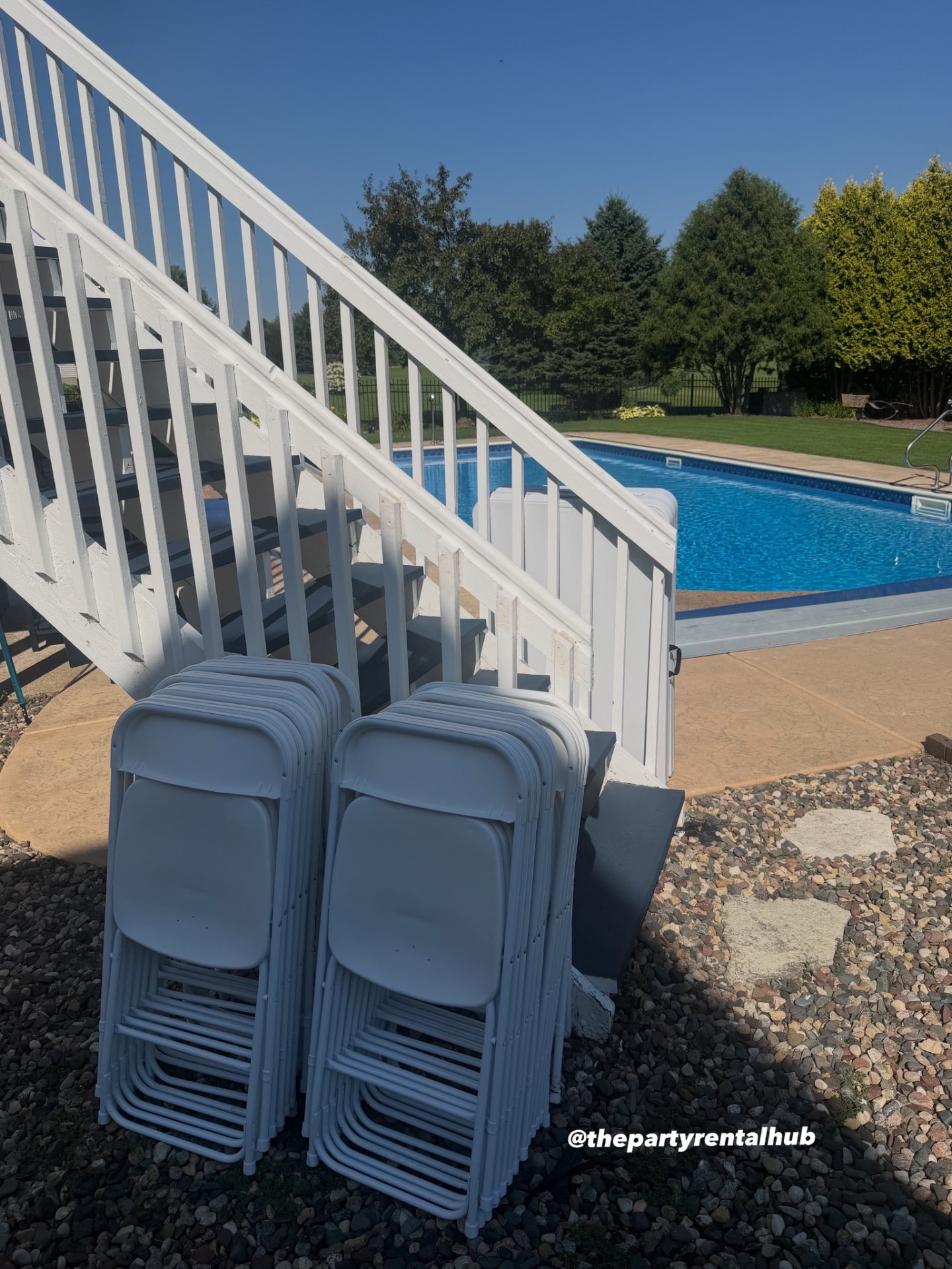 Stacks of white folding chairs delivered next to a backyard pool
